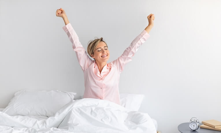 žena se po probuzení s úsměvem protahuje na posteli