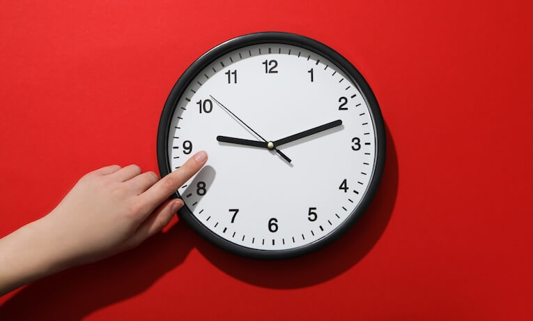 ruka ukazující na hodiny na červené zdi