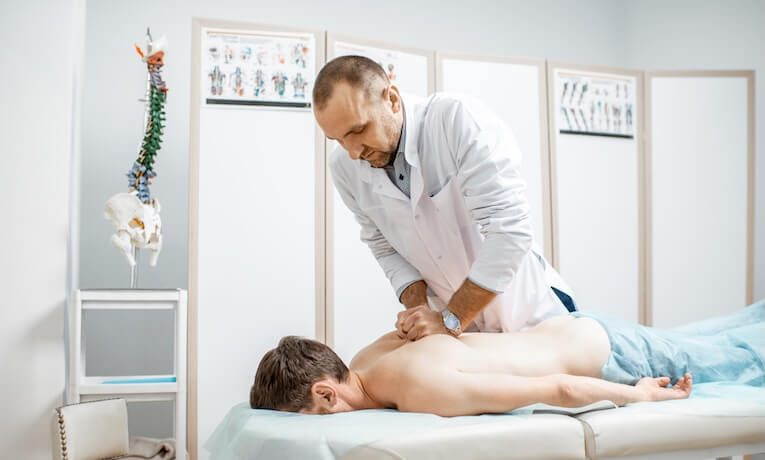 lékař masíruje záda muži ležícímu na masážním stole