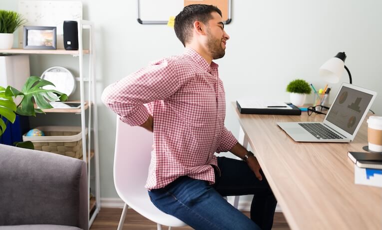 mladý muž pracující na notebooku s bolestmi zad