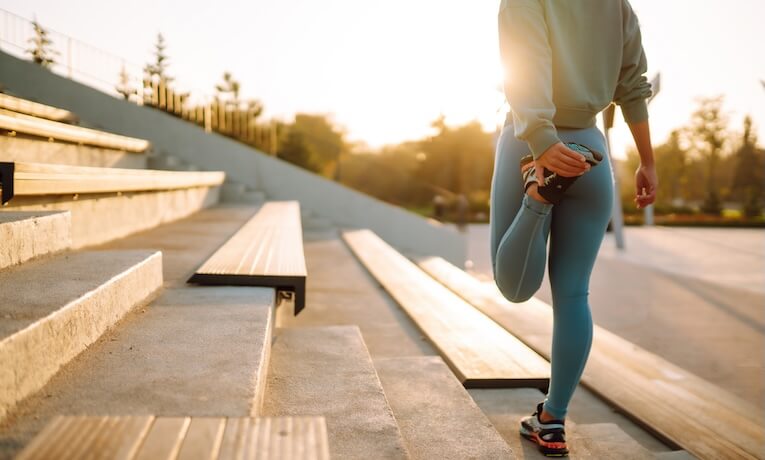 žena v legínách a teniskách si natahuje nohu