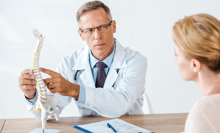 lékař pacientce vysvětluje pomocí modelu páteře