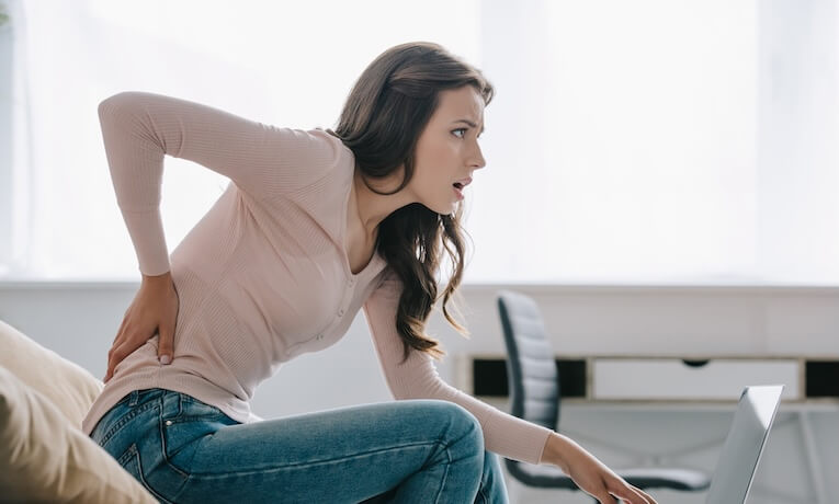 mladá žena pracující na notebooku s bolestí v bedrech