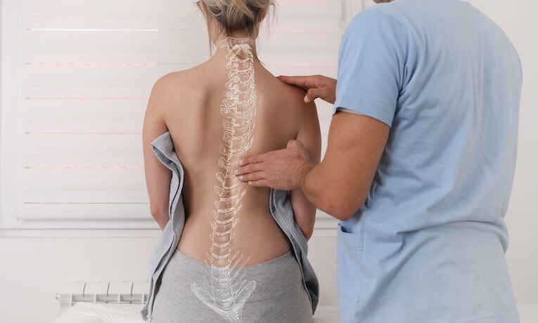 lékař vyšetřuje záda mladé ženy, na nichž je graficky vyznačena páteř