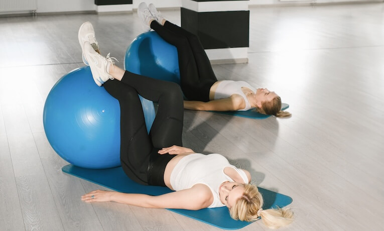 dvě mladé ženy cvičí na fitness míči v tělocvičně