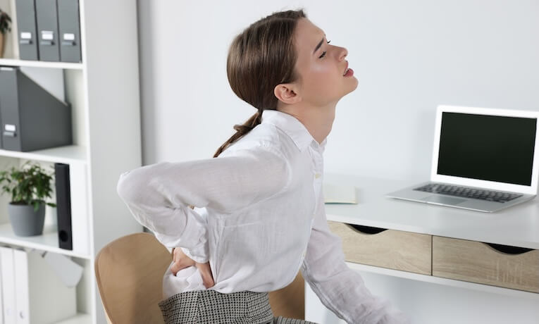 mladá žena pracující na notebooku má bolesti v bederní oblasti