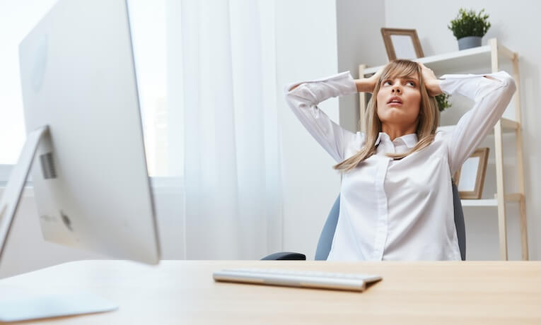 mladá žena pracující na počítači si drží oběma rukama hlavu