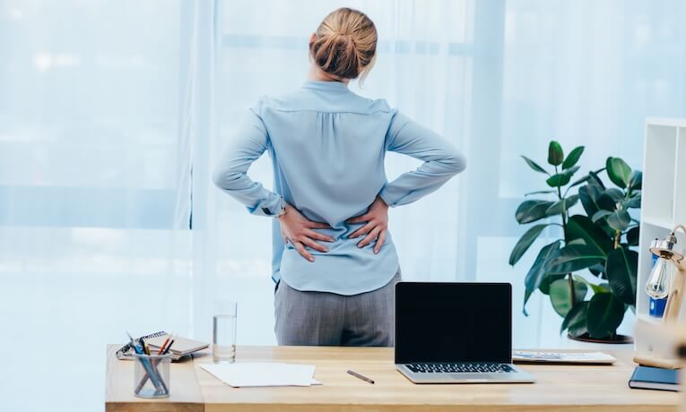 žena v kanceláři stojí u okna a drží si rukama bedra