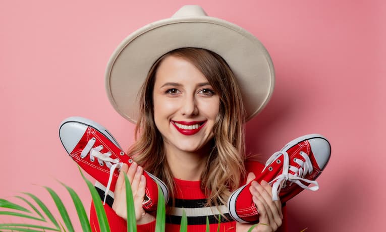 mladá žena drží v každé ruce jednu červenou tenisku