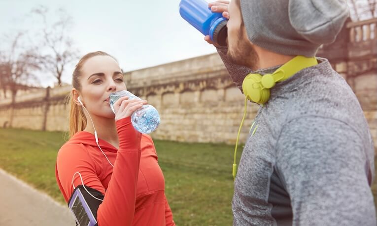 muž a žena ve sportovním oblečení se sluchátky pijí z lahví