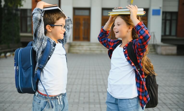školáci, chlapec a dívka, s batohy na zádech a knihami na hlavách