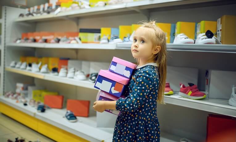holčička v obchodě s obuví nese tři krabice s botami