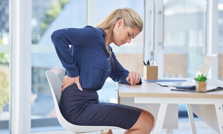 žena pracující na notebooku s bolestmi v oblasti kříže
