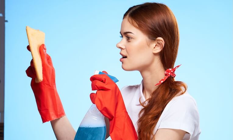 mladá žena v gumových rukavicích drží hadřík a čisticí prostředek