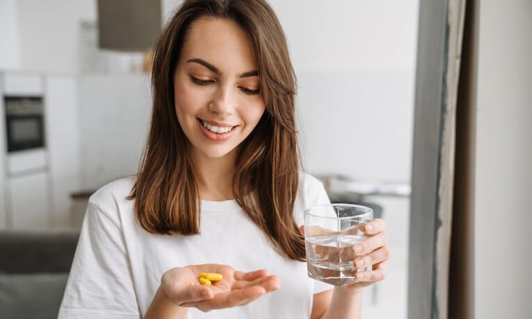 mladá žena se chystá vypít tři žluté kapsle