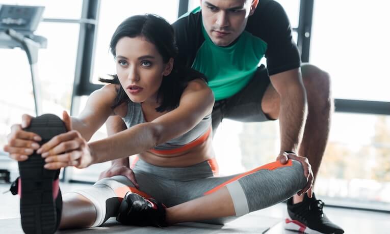 mladá žena se pod dohledem trenéra protahuje